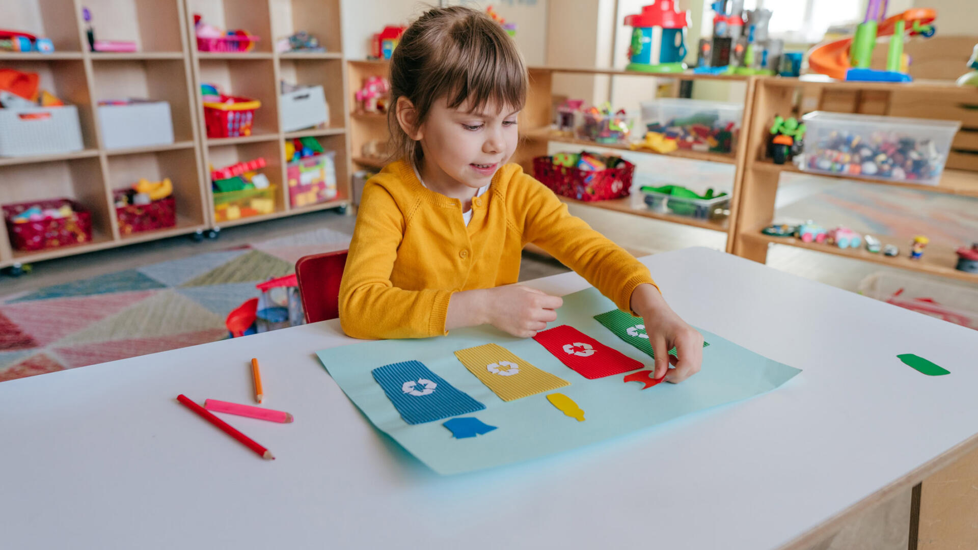 A little girl sitting at a table in a playroom.